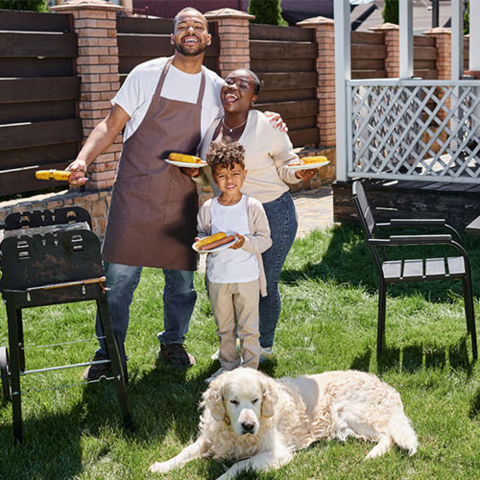 Family in back yard posing in front of a grill with a golden retriever.