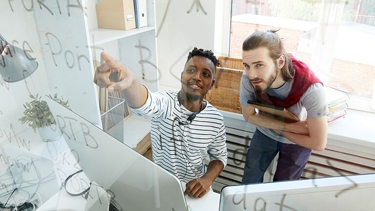 two men looking at note they have written on a glass window 