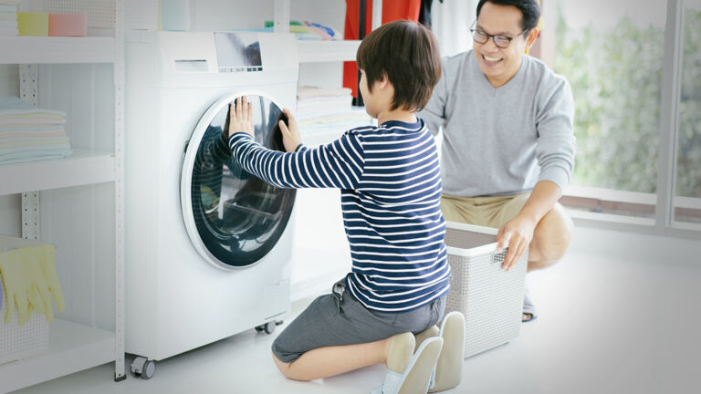 woman closing the door to a washing machine while her husband kneels next to her helping her and load it