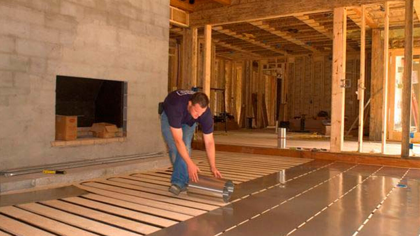 Man rolling out aluminum flooring material onto floor of new construction.