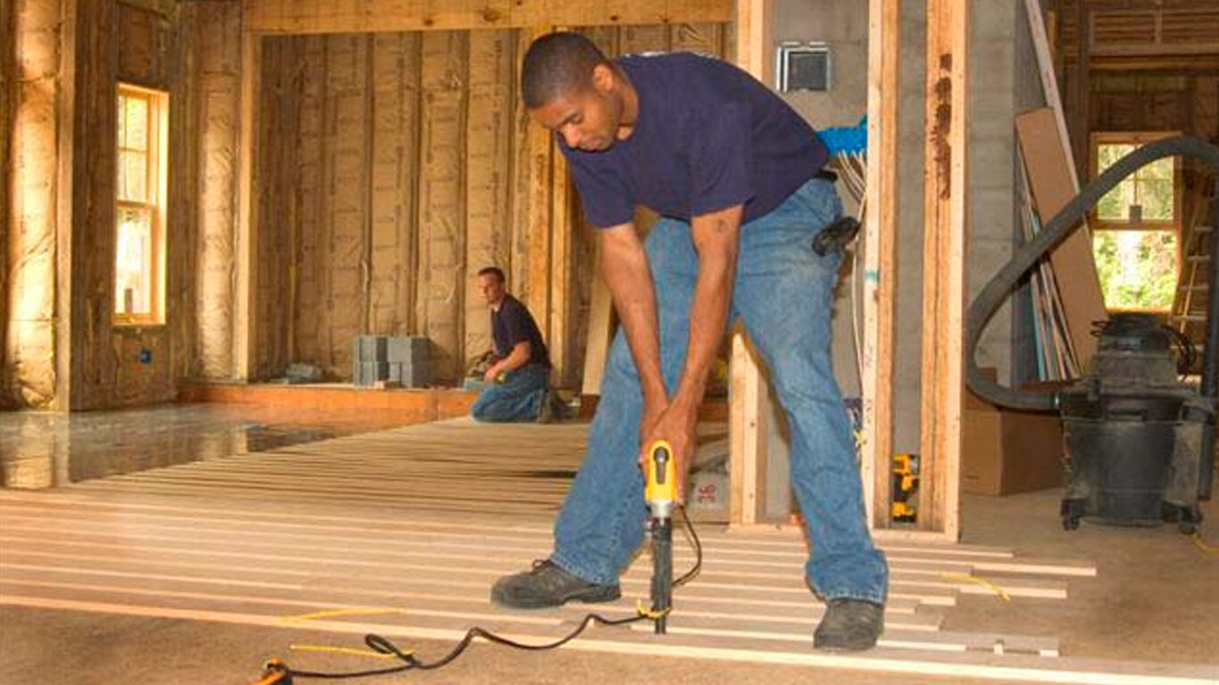 Workers installing flooring onto new house construction.