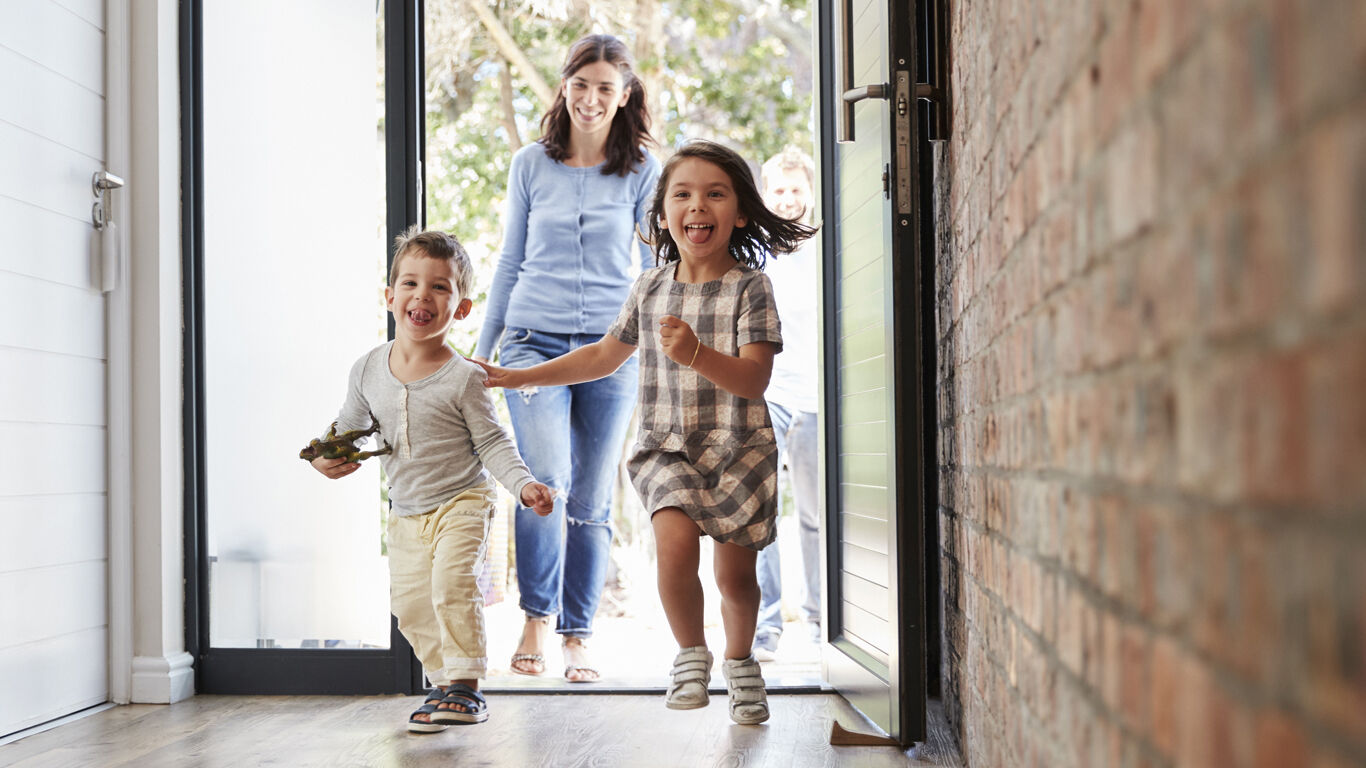 A little girl and boy running into the house with excitement Infront of their Mom