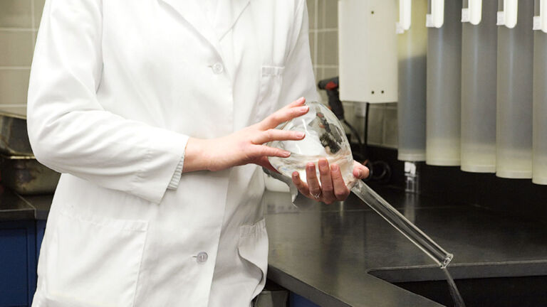 Lab technician emptying beaker of fluid