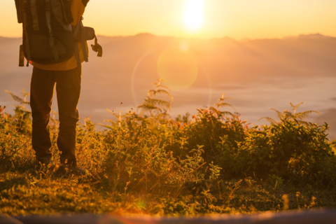 hiker-stand-camping-near-orange-tent-backpack-mountains